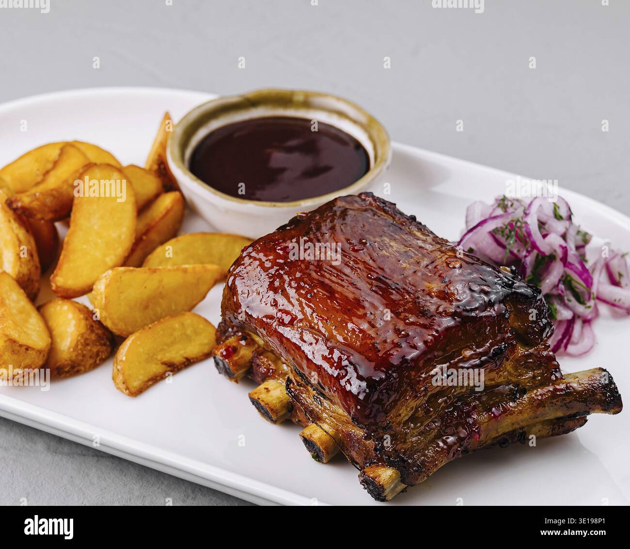 Köstlicher Teller mit glasierten Schweinerippchen mit Kartoffelscheiben, bbq-Sauce und Slaw auf einem weißen Teller Stockfoto