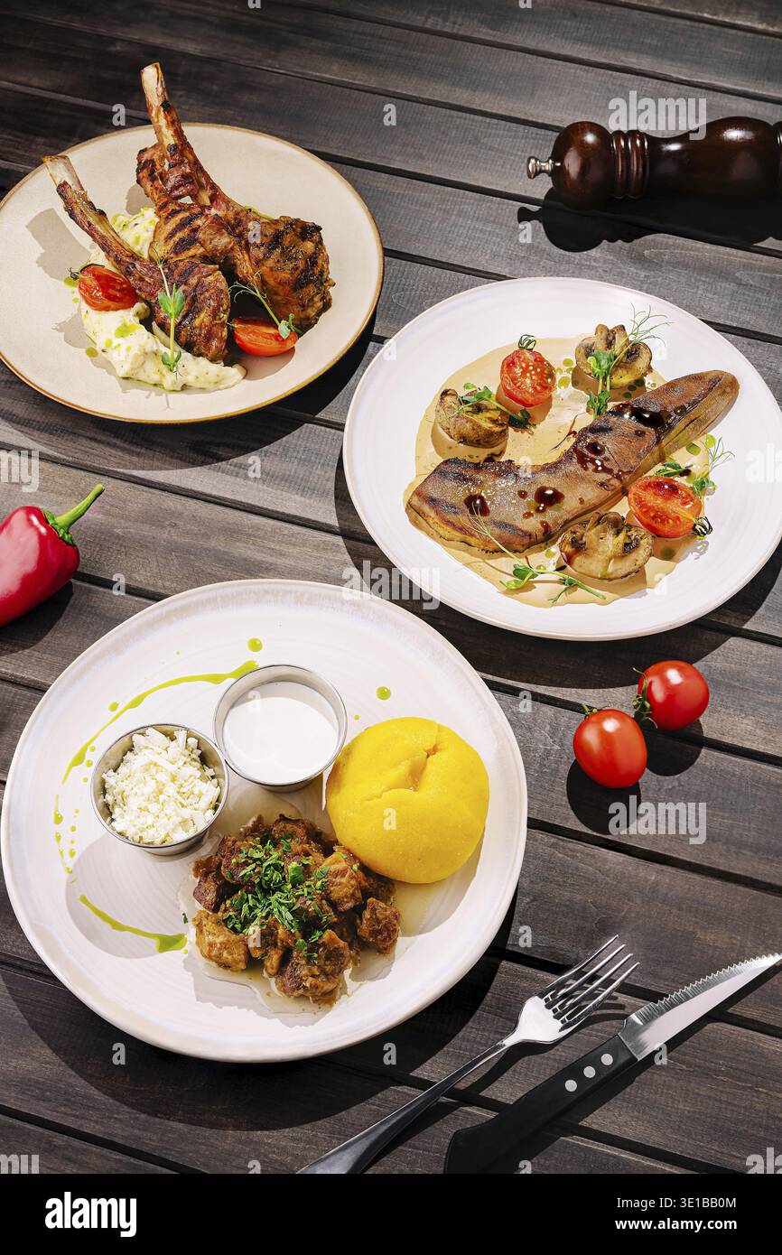 Köstliche Teller mit gegrilltem Lammkotelett, cremigem Kartoffelpüree und gefüllten Knödeln werden an einem rustikalen Holztisch serviert, um ein köstliches Fu zu kreieren Stockfoto