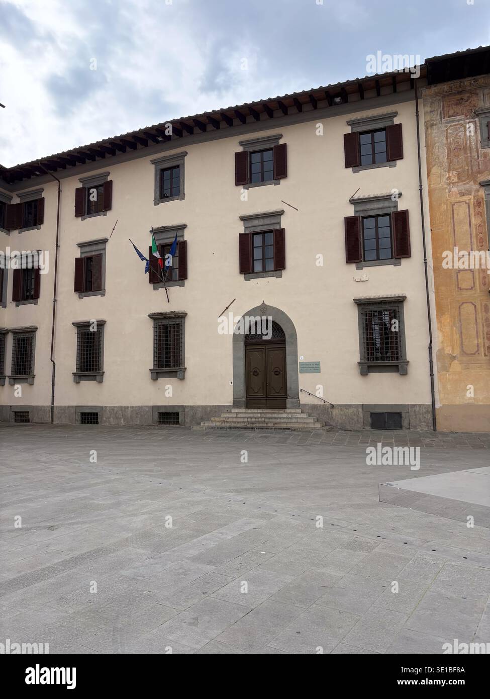 Biblioteca Del Dipartimento Di Diritto Pubblico. Pisa, Italien. Institutionelles Gebäude mit Fensterläden und italienischen Fahnen, die unter einem bewölkten Himmel fliegen Stockfoto