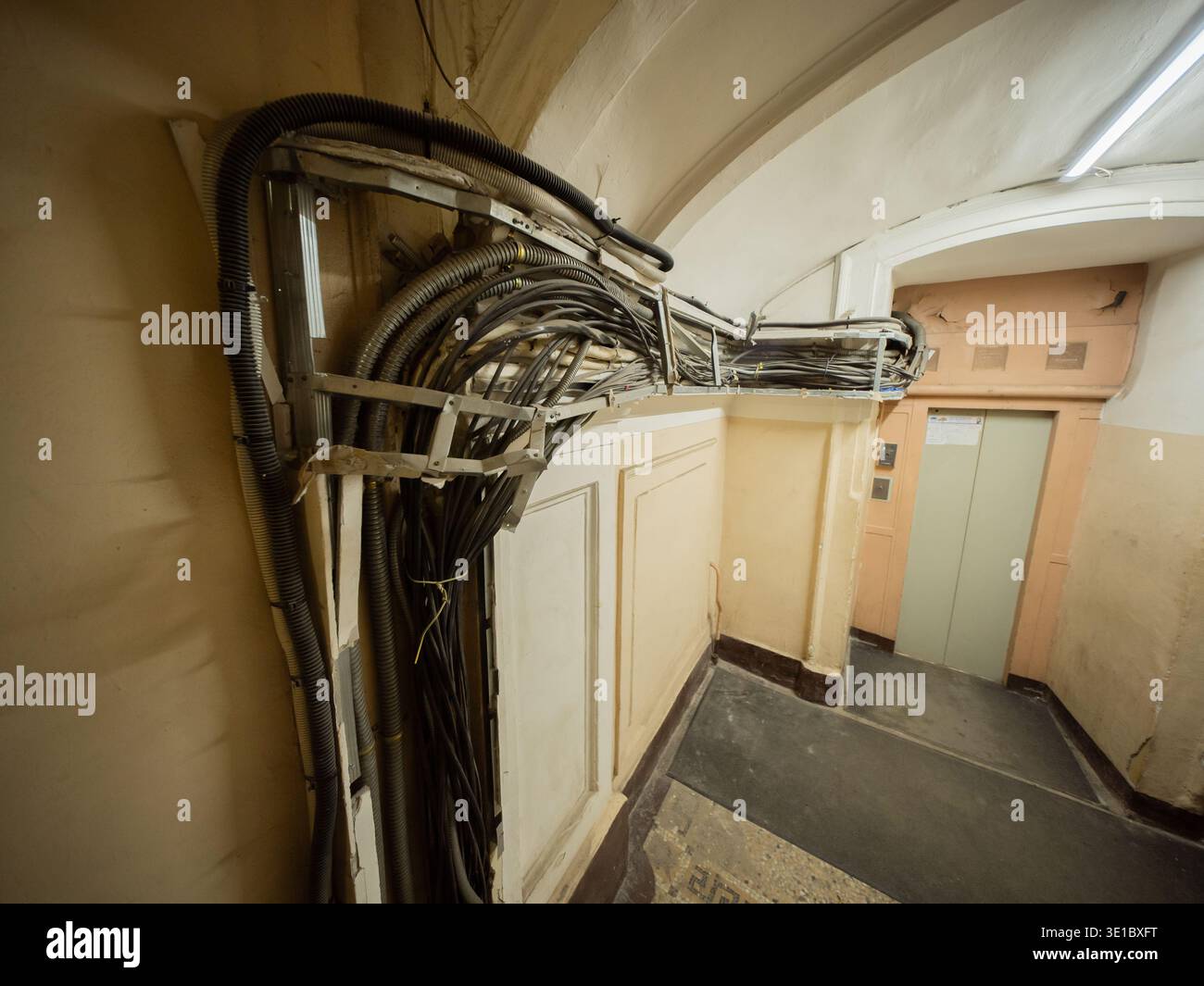 Freiliegende Kabel und Elektrodrähte, die entlang eines alten Gebäudeflurs verlaufen Stockfoto