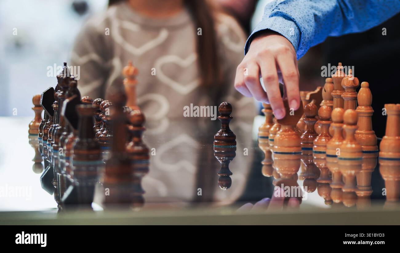 Handbewegung eines weißen Bauern auf einem reflektierenden Schachbrett während eines Schachspiels Stockfoto