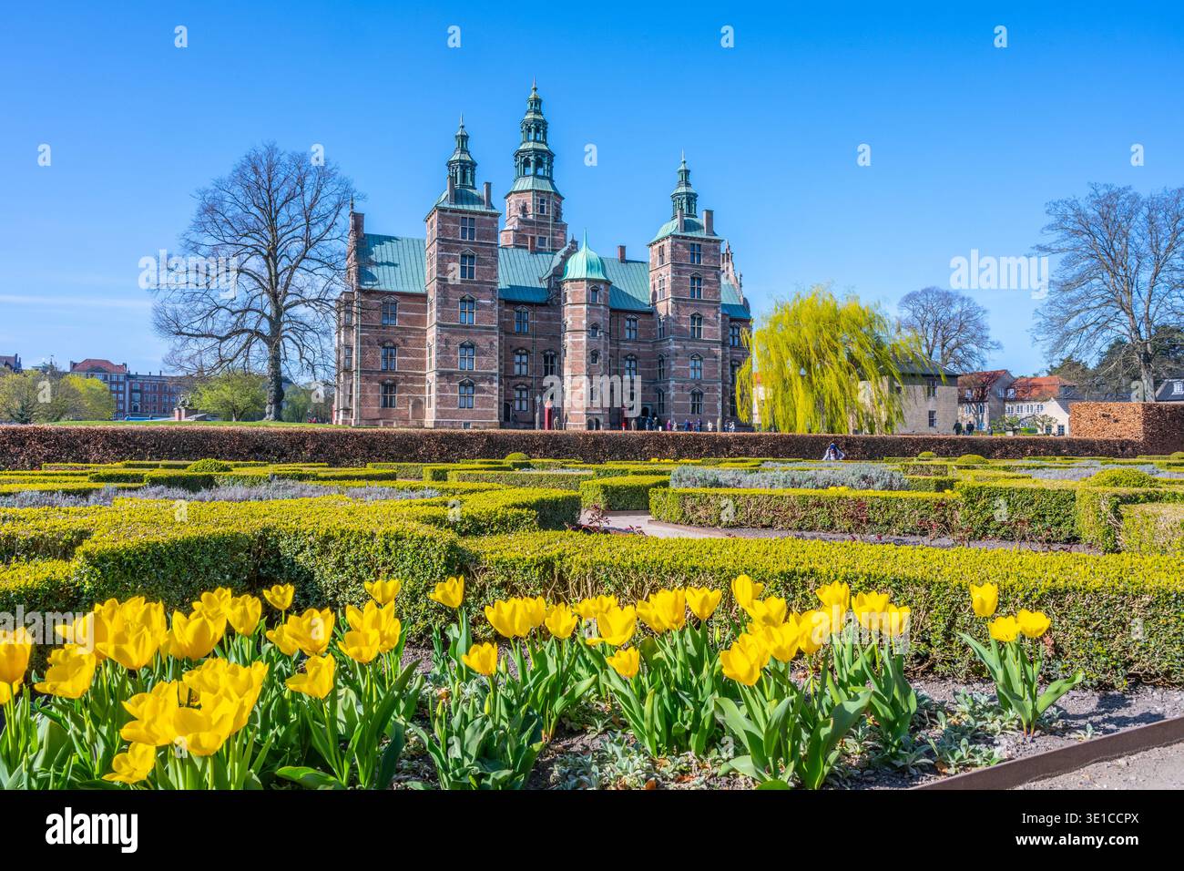 Schloss Rosenborg steht majestätisch in Kopenhagen, Dänemark, umgeben von leuchtend gelben Tulpen und üppigem Grün. Besucher genießen die ruhige Atmosphäre an einem klaren Frühlingstag. Stockfoto