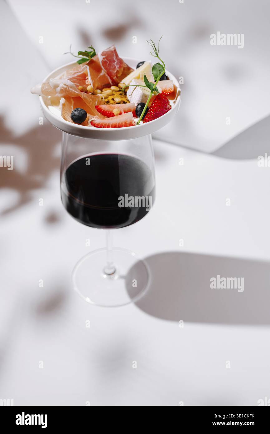 Elegantes Rotweinglas mit Wurstwaren, Früchten, Käse und Nüssen - eine raffinierte Kombination, die perfekt für Gourmetversammlungen oder gehobene Weinproben geeignet ist Stockfoto