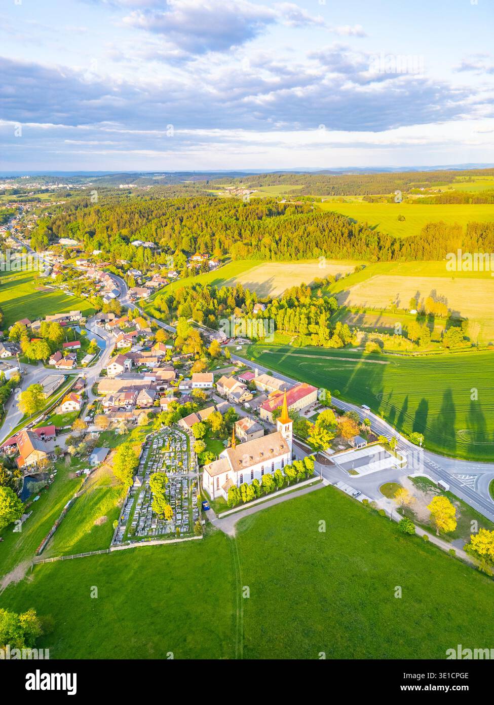 Bohutin Town bietet eine malerische Landschaft mit üppigen Feldern und malerischen Häusern. Die historische Kirche und der Friedhof sind markante Elemente, die vom warmen Glanz des Sonnenuntergangs beleuchtet werden. Stockfoto