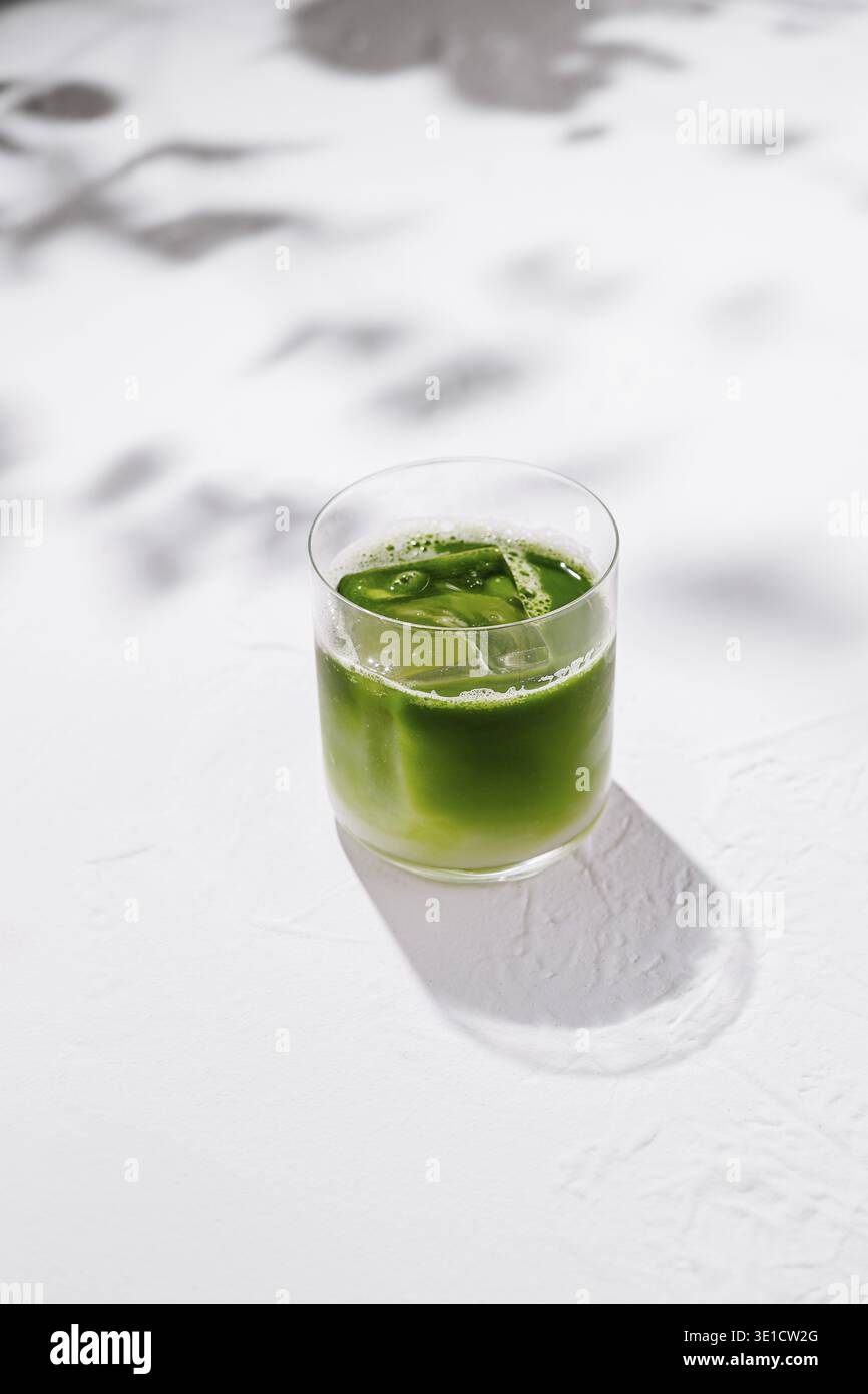 Erfrischende Eismatcha Latte sitzt auf einem weißen Tisch mit Schatten von Blättern im Hintergrund Stockfoto