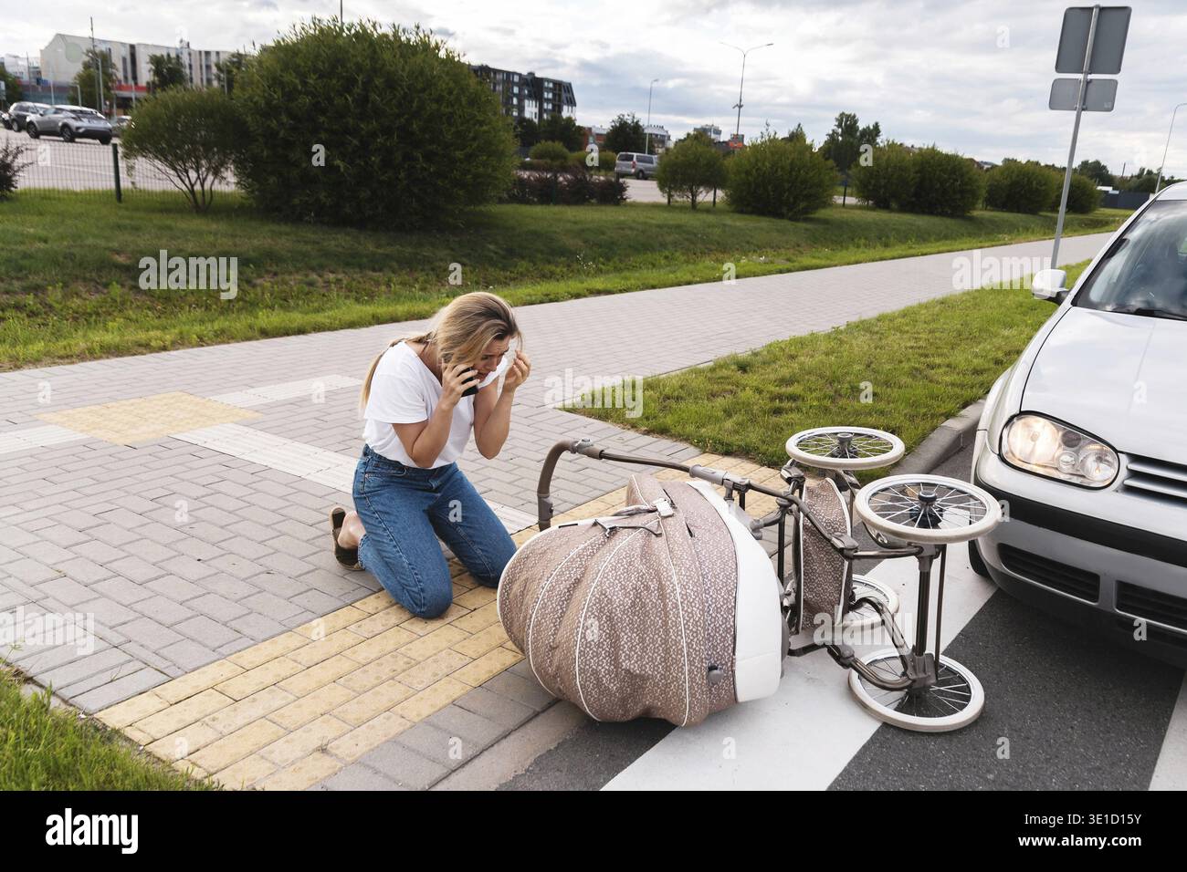 Schockierte Mutter macht einen Notruf auf dem Fußweg nach einem Autounfall, als ein Fahrzeug ihren Kinderwagen trifft. Sicherheitskonzepte, Verkehrsordnung und i Stockfoto
