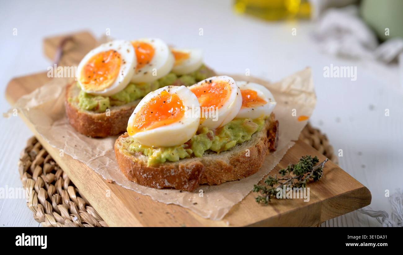 Zwei Scheiben knuspriges Sauerteigbrot, garniert mit cremiger Guacamole und weichen, gekochten Eierhälften. Warmes natürliches Licht unterstreicht den lebendigen Orang Stockfoto
