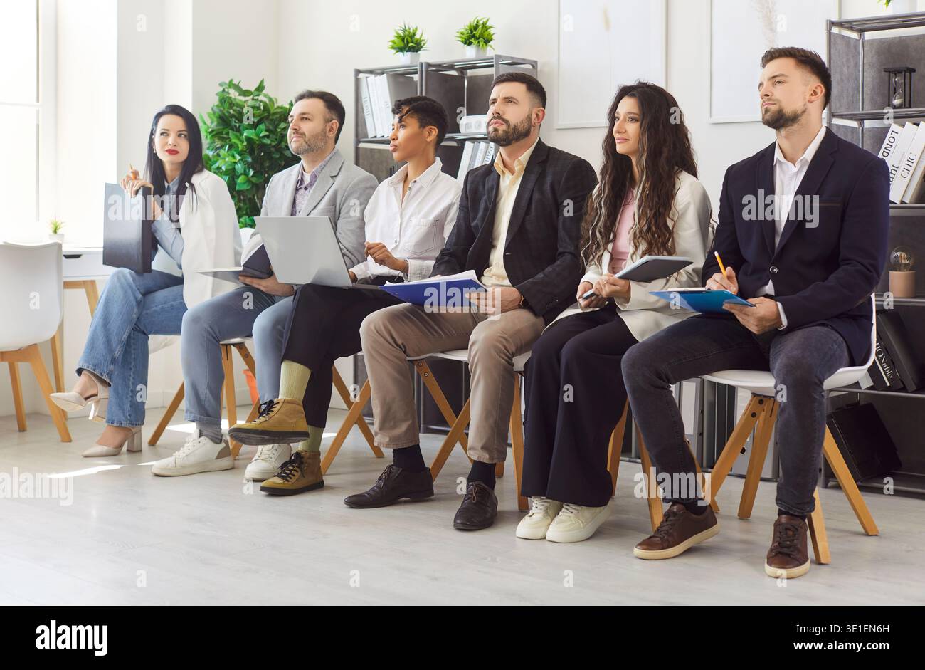 Junge Geschäftsleute, die beim Treffen im Büro hintereinander sitzen und ihren Kollegen zuhören Stockfoto