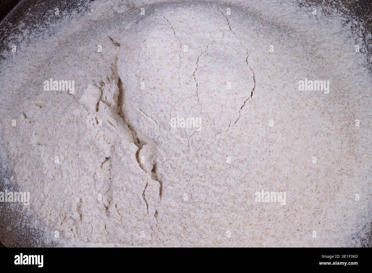 Vollkornmehlhügel für gesundes Backen, grobe Textur mit sichtbaren Kleieflecken auf Holztablett, gesunde rustikale Atmosphäre, nahrhafte Zutat Stockfoto