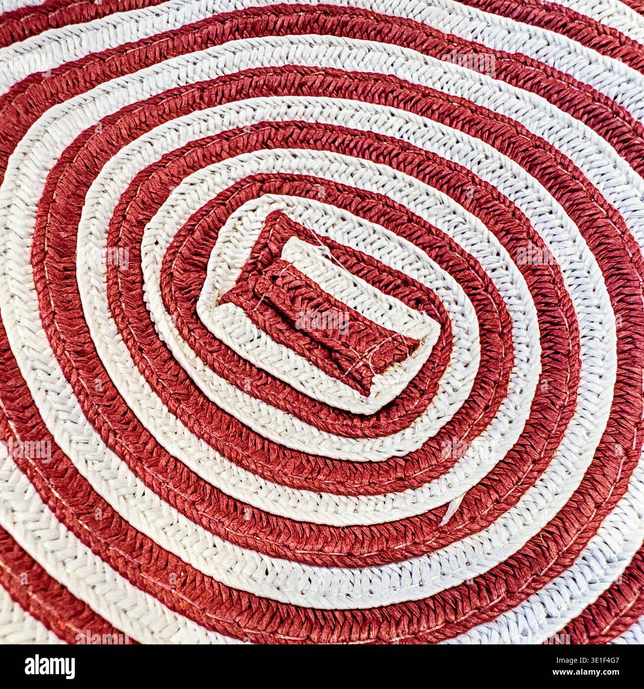 Ein rot-weißes geometrisches Spiralmuster ist Teil eines gewebten Korbs. Stockfoto