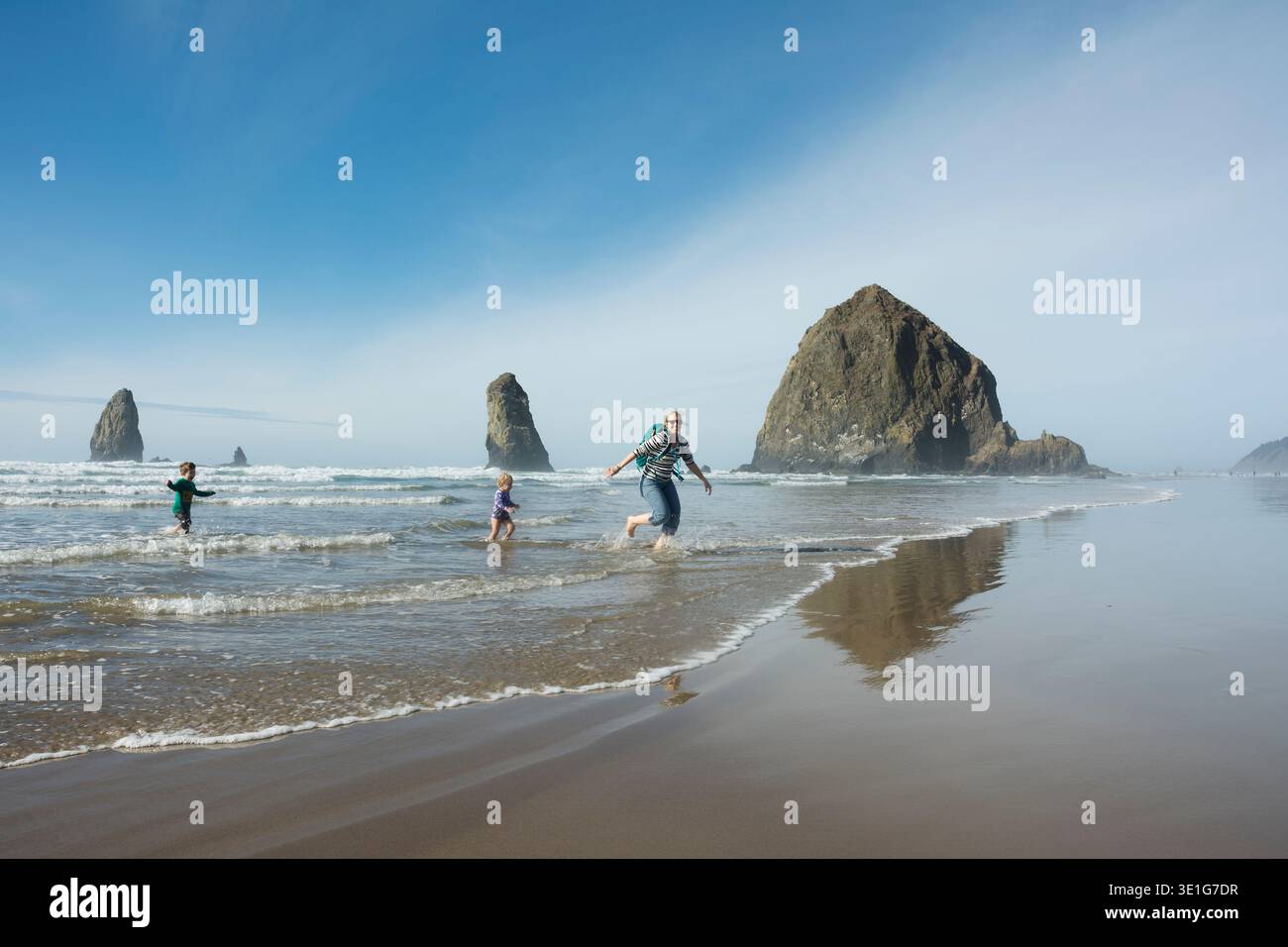 Mutter, Sohn und Tochter laufen vor dem Haystack Rock am Cannon Beach, Oregon. Stockfoto