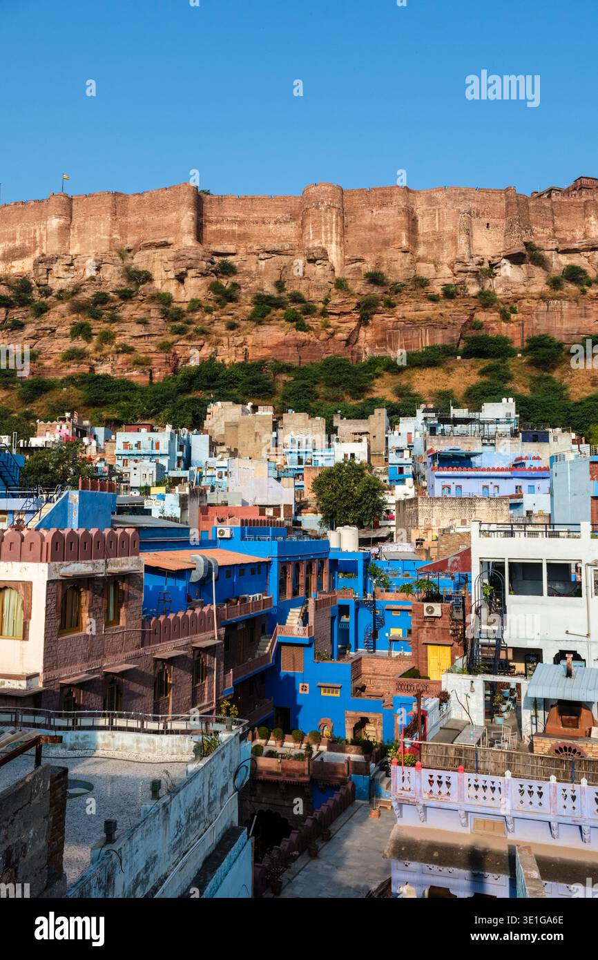 Hell bemalte blau-weiße Häuser von Jodhpur stehen am Fuße der steilen Klippe, die den weitläufigen Mehrangarh Fort Komplex stützt. Stockfoto