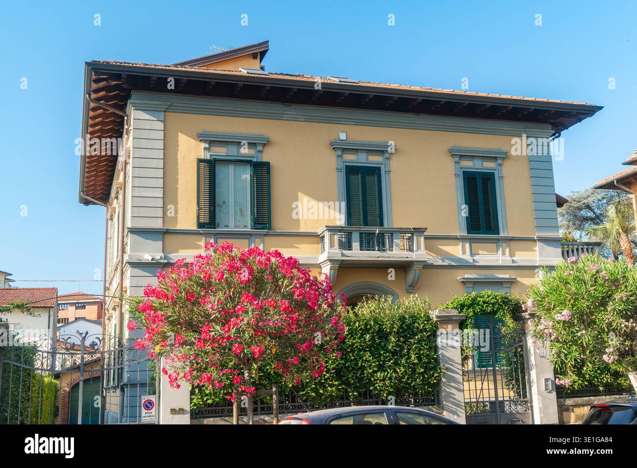 Italienische Hausfassade mit blühenden rosafarbenen Blumen und grünen Fensterläden. Heller Sommertag und mediterrane Lifestyle-Atmosphäre. Stockfoto