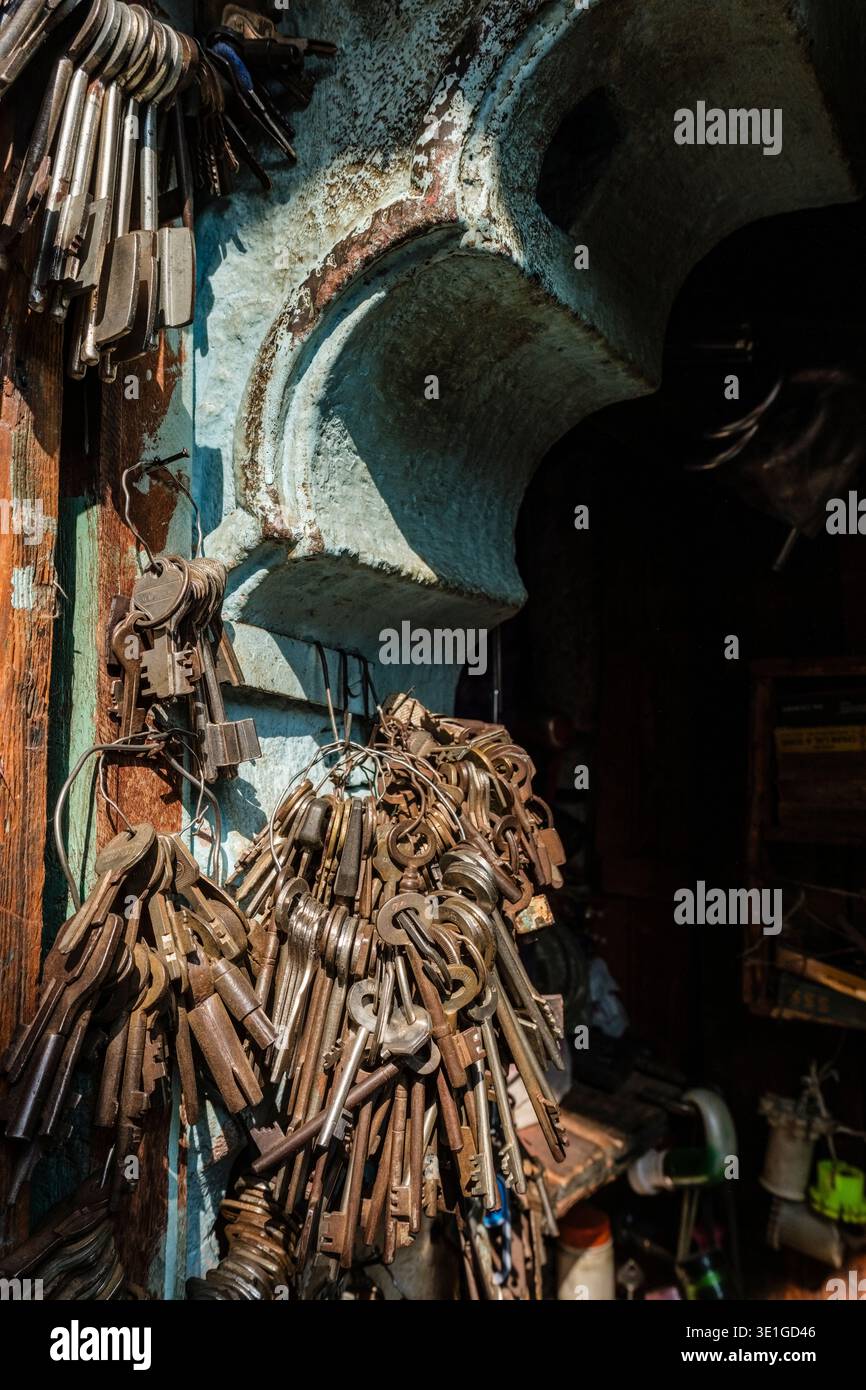 Große Bündel alter eiserner Schlüssel hängen an Drahtschlaufen an einer verwitterten türkisfarbenen Wand in einer traditionellen Schlosserei in Jodhpur. Stockfoto