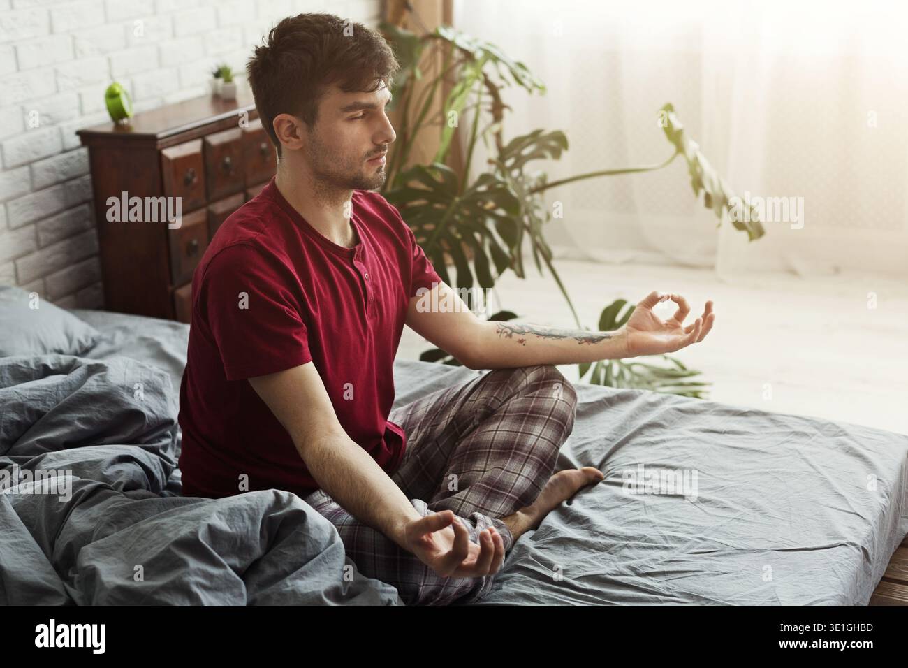 Junger Mann sitzt im Bett in Lotusposition Stockfoto