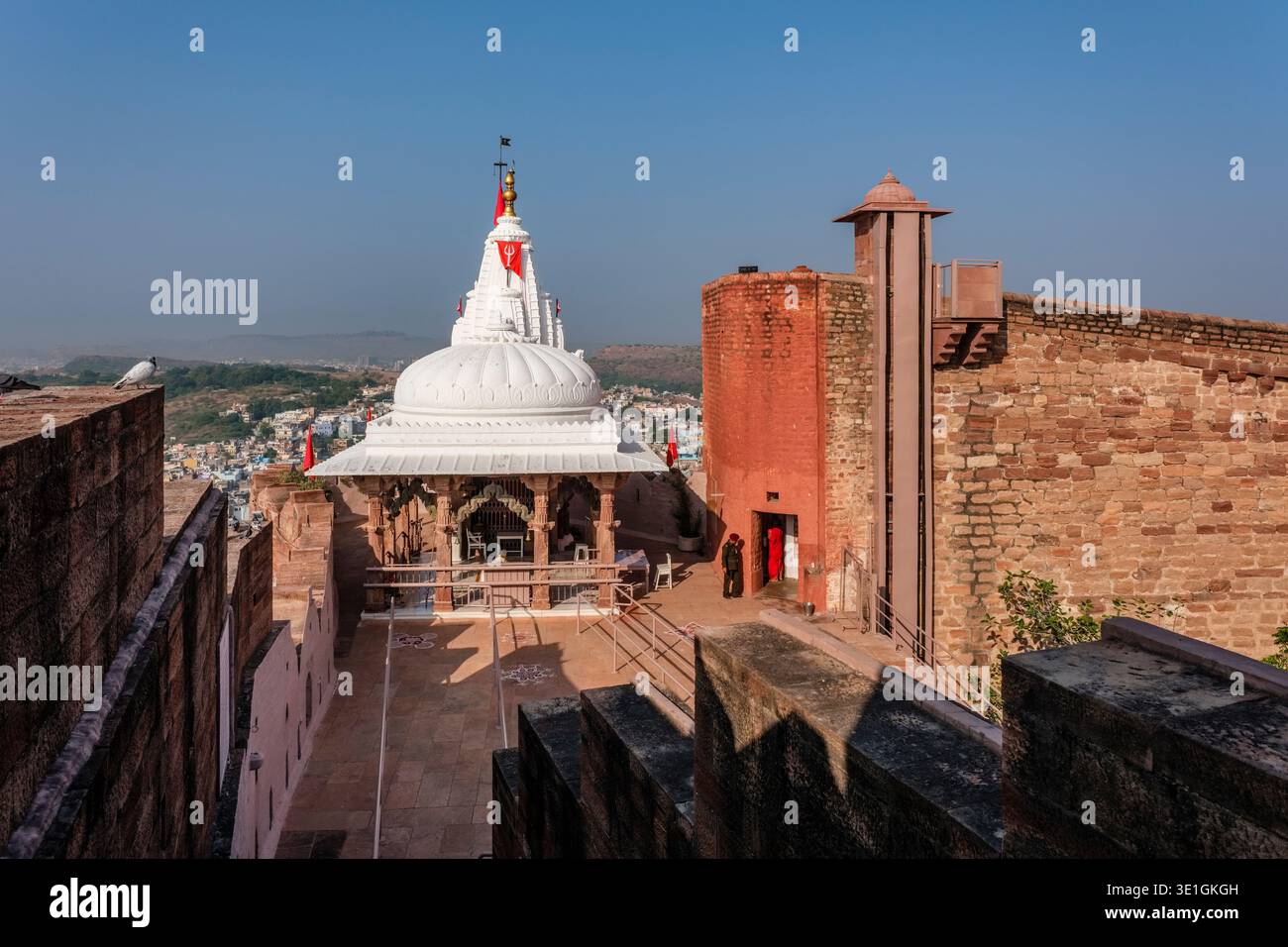 Der Chamunda Mataji Tempel im Mehrangarh Fort in Jodhpur überblickt die Blaue Stadt in der Ferne mit ihren charakteristischen weißen Kuppeln und Fahnen. Stockfoto