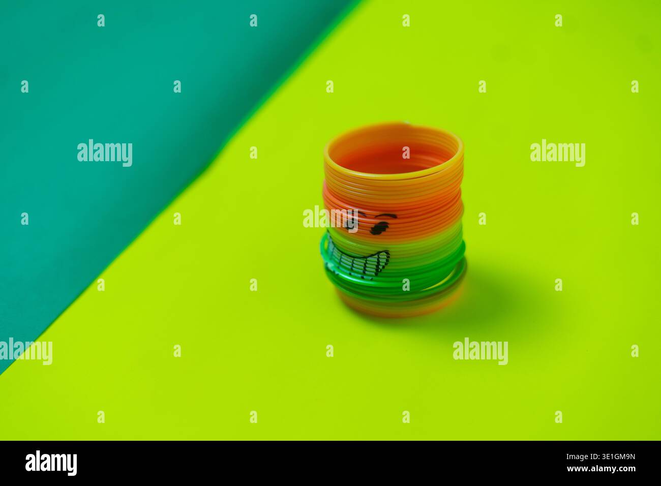 Ein lebhaftes, regenbogenfarbenes Frühlingsspielzeug mit einem fröhlichen, handgezeichneten Smiley-Gesicht sitzt auf einem hellgrünen Hintergrund. Dieses spielerische Objekt erinnert an Kindheit Nein Stockfoto