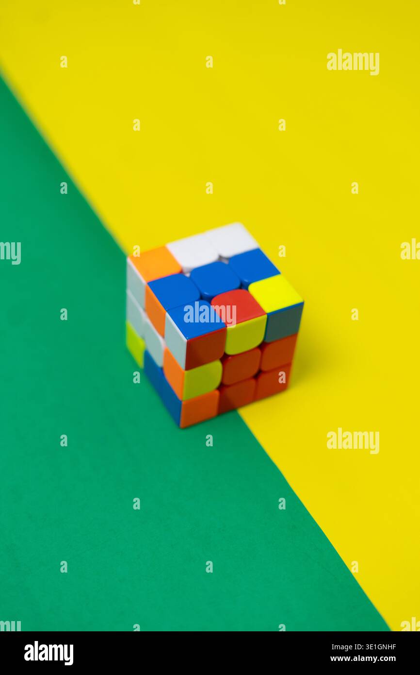 Ein farbenfroher Logikpuzzle-Würfel sitzt auf einem lebendigen diagonalen Hintergrund aus gelb und grün und steht für Problemlösung, Kreativität und mentale Herausforderung. Stockfoto