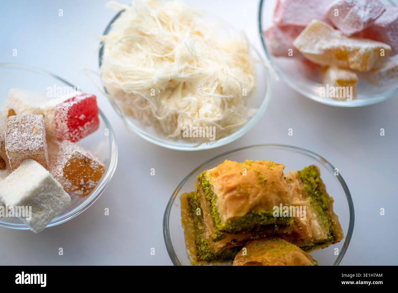 Verschiedene Arten von Süßigkeiten sind in Schüsseln auf einer weißen Oberfläche angeordnet. Zu den Süßigkeiten gehören bunte Würfel, geschreddertes Gebäck und mehrschichtige Desserts. Stockfoto