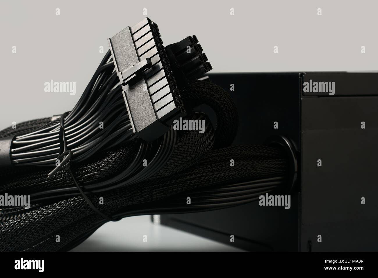 Schwarzer 24-poliger atx-Hauptplatinenanschluss und gebündelte Kabel mit Netzmantel vom pc-Netzteil isoliert grauer Hintergrund, Seitenansicht Nahaufnahme Stockfoto