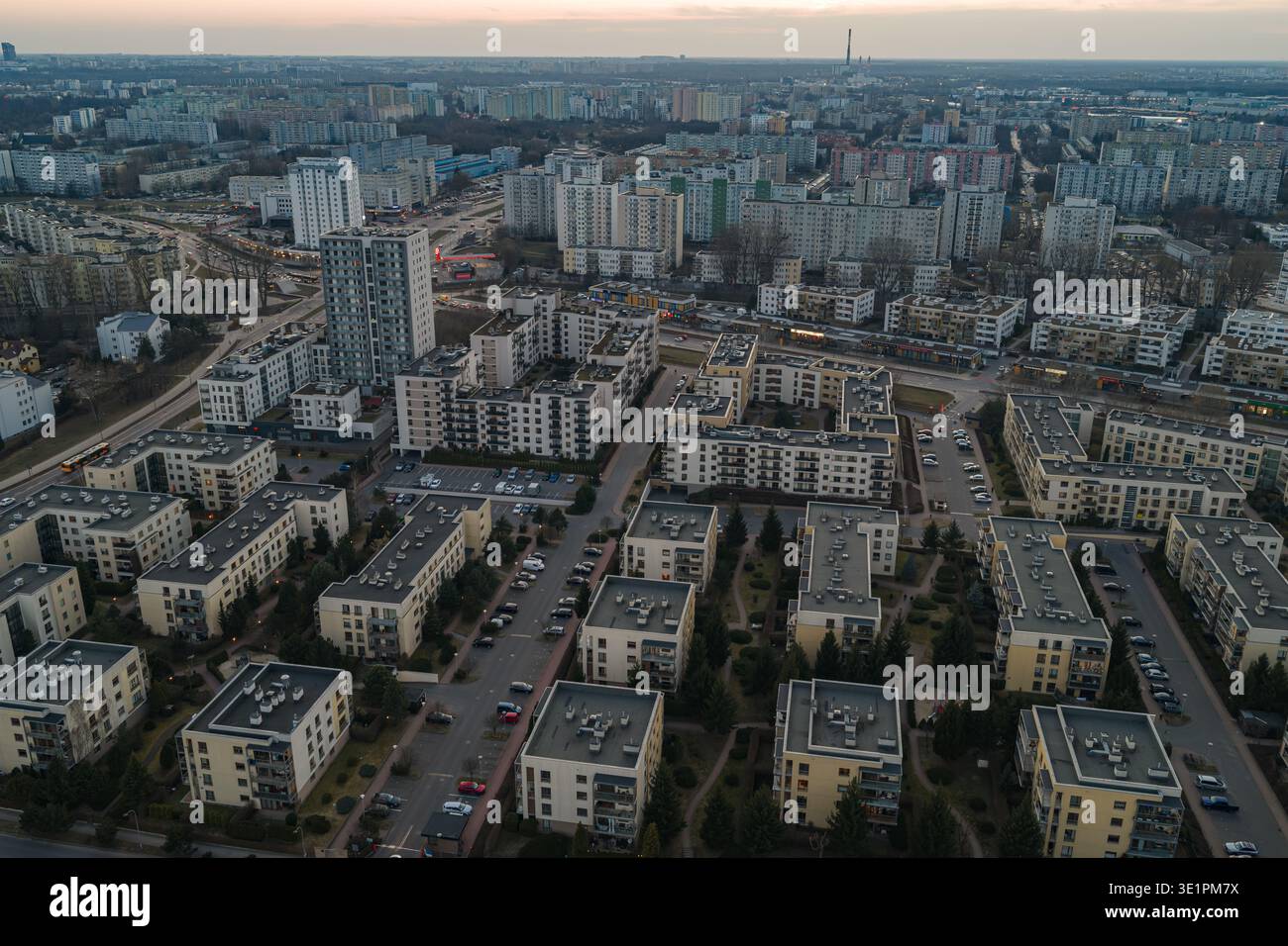 Aus der Vogelperspektive von Warschau, Polen, in der Abenddämmerung sind mittelhohe Blöcke, Innenhöfe und von Bäumen gesäumte Straßen zu sehen. Autolampen zeichnen Straßen ab, mit dem Kulturpalast A Stockfoto