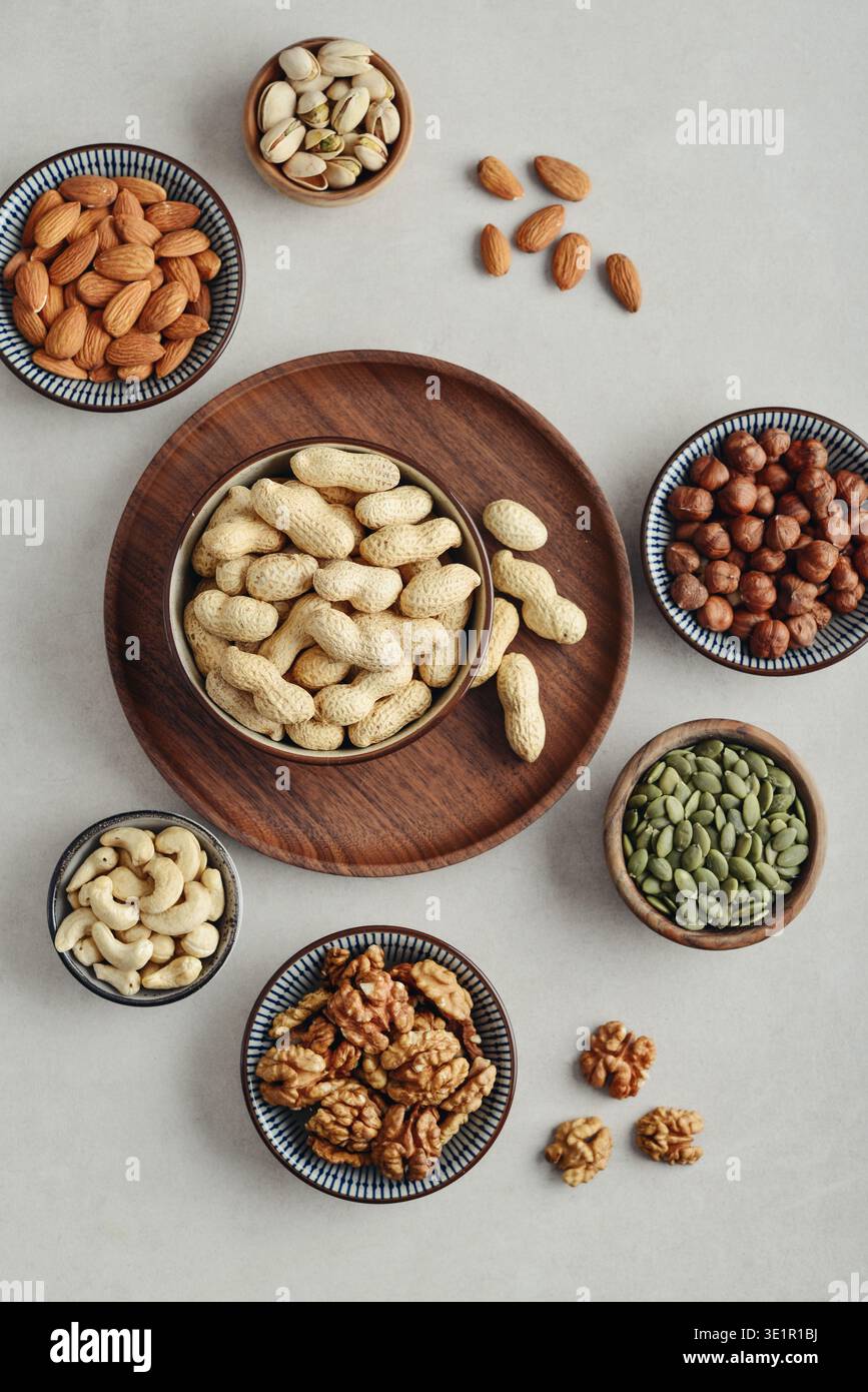 Walnüsse, Cashewnüsse, Mandeln, Haselnüsse, Erdnüsse, Pistazien und Kürbiskerne in Tellern auf hellem Hintergrund, Draufsicht Stockfoto