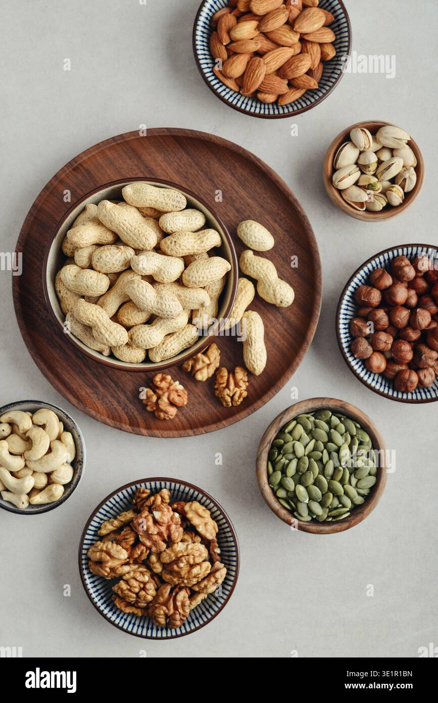Walnüsse, Cashewnüsse, Mandeln, Haselnüsse, Erdnüsse, Pistazien und Kürbiskerne in Tellern auf hellem Hintergrund, Draufsicht Stockfoto