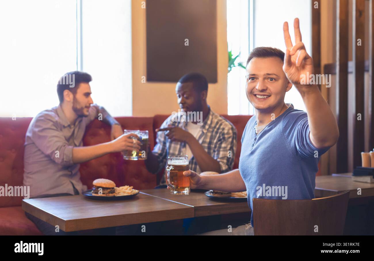 Aufgeregt, junger Kerl Bestellung mehr Bier, ruht mit Freunden an der Bar Stockfoto