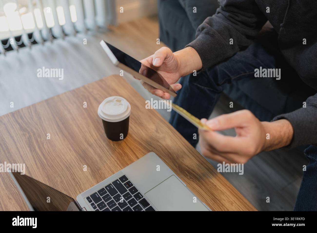 Mann mit Kreditkarte und Smartphone in der Nähe eines Laptops für Online-Zahlungen und digitales Banking, repräsentiert E-Commerce-Transaktionen und moderne Finanzen Stockfoto