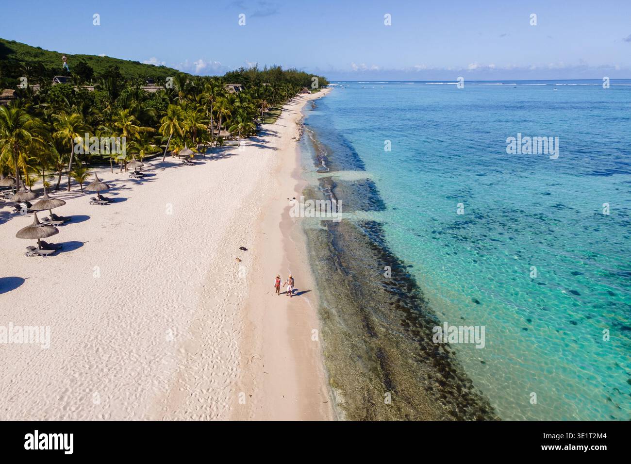 Ein Paar genießt einen ruhigen Spaziergang am unberührten Strand von Mauritius, umgeben von Palmen und atemberaubendem türkisfarbenem Wasser unter einem hellblauen Himmel. Ein paar Spaziergänge am Le Morne Beach auf Mauritius Stockfoto
