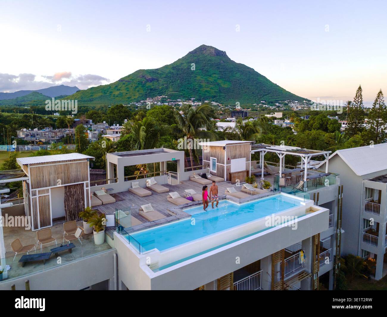 Entspannung trifft Schönheit in einem luxuriösen Pool in Rivire Noire, Mauritius. Ein Paar genießt einen ruhigen Moment, während die Sonne über den üppigen Bergen und dem pulsierenden Himmel untergeht und eine perfekte Urlaubsatmosphäre schafft. Stockfoto