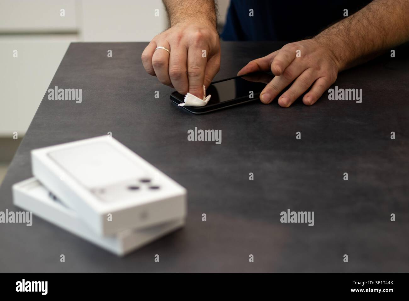 09.20.2025: Flensburg, Deutschland. Mann, der die Bildschirmoberfläche eines neuen Apple iPhone 17pro max mit einem Tuch auf einem dunkelgrauen Tisch reinigt Stockfoto