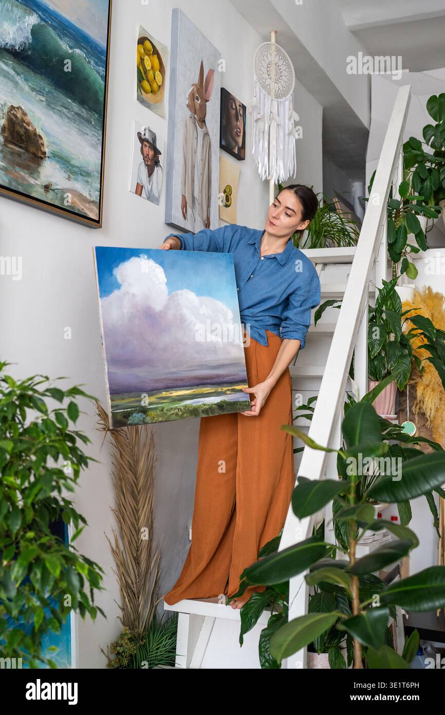 Stolze talentierte Künstlerin posiert in der Loft-Galerie auf Treppen mit fertigem Kunstwerk. Stockfoto