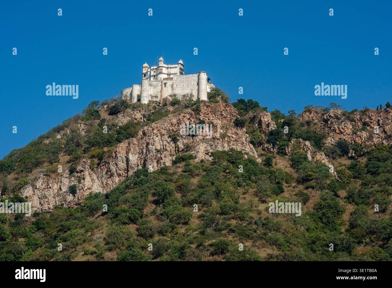 Der historische Monsoon-Palast in Udaipur steht auf einem steilen, felsigen Hügel, der von grüner Vegetation bedeckt ist, vor einem klaren blauen Sommerhimmel. Stockfoto