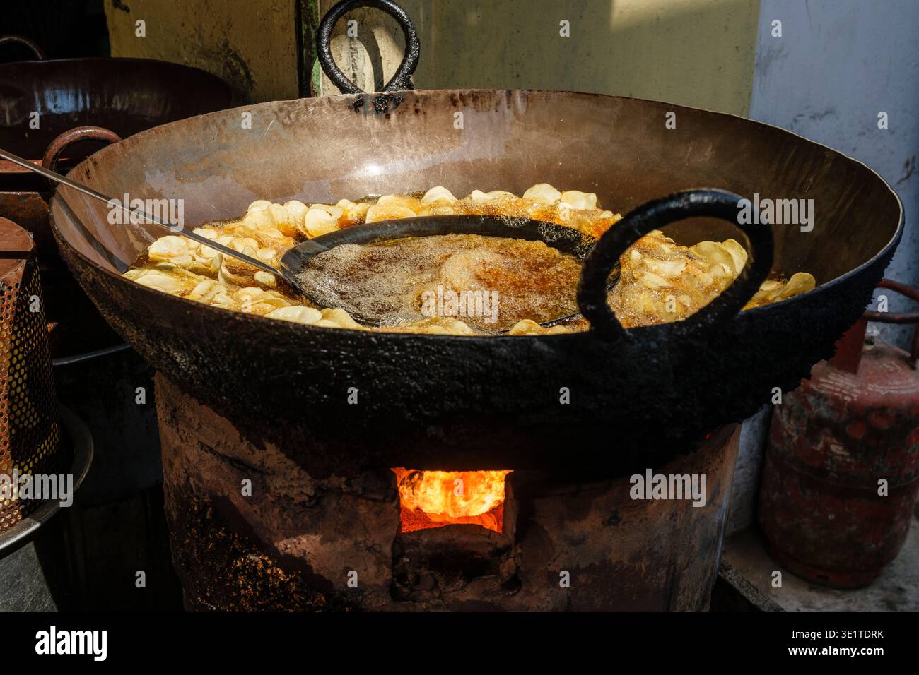 Große Metallpfannen gefüllt mit dünnen Kartoffelscheiben brutzeln in heißem Öl über einem offenen Holzofen in einer traditionellen Außenküche in Udaipur. Stockfoto