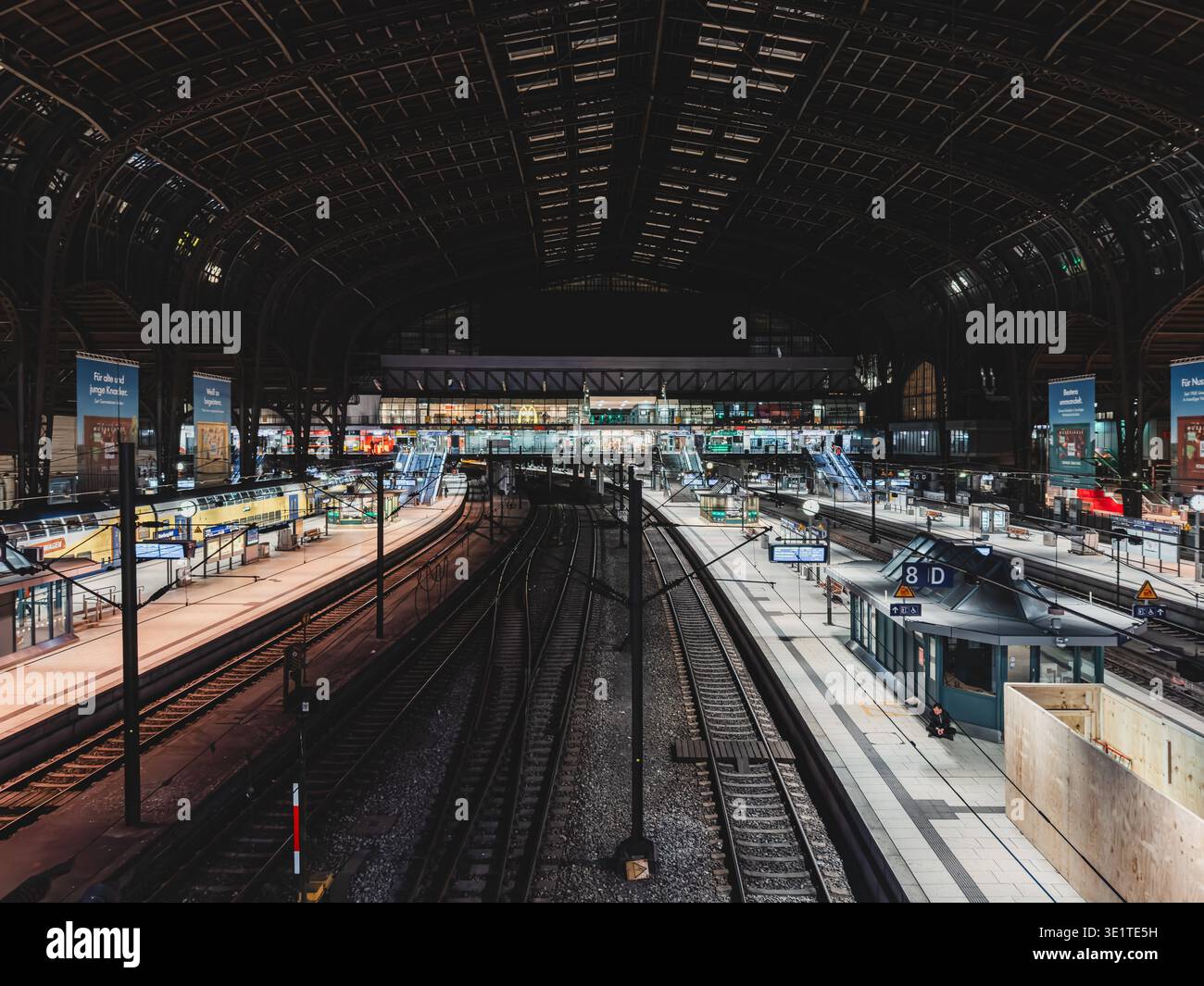 Deutschland, Hamburg: Bahnsteige und Gleisanlagen im Hamburg Hauptbahnhof, große Bahnhofshalle mit Stahlkonstruktion und gewölbtem Dach, nächtliche Stimmung mit künstlicher Beleuchtung, wenig Verkehr, kaum Reisende auf den Bahnsteigen, weitgehend leere Gleise, ruhiger Moment im sonst stark frequentierten Verkehrsknotenpunkt, Farn- und Regionalverkehrsinfrastruktur, zentrale Drehscheibe des Bahnverkehrs im Norden Deutschlands, historische Hallenarchitektur kombiniert mit moderner Technik, klare Linienführung der Gleise als grafisches Element, dokumentarische Stadt Stockfoto