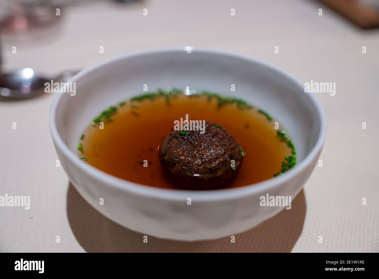 Minimalistischer Bernsteinkonsomme mit Trüffelknödel in weißer Schüssel Stockfoto