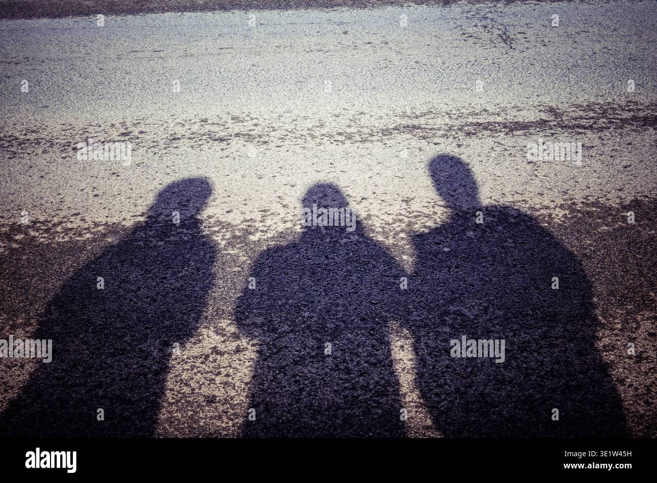 Schattensilhouette auf hell beleuchtetem, nassem Pflaster des Oberkörpers von drei Menschenfiguren, die Schulter an Schulter stehen. Stockfoto