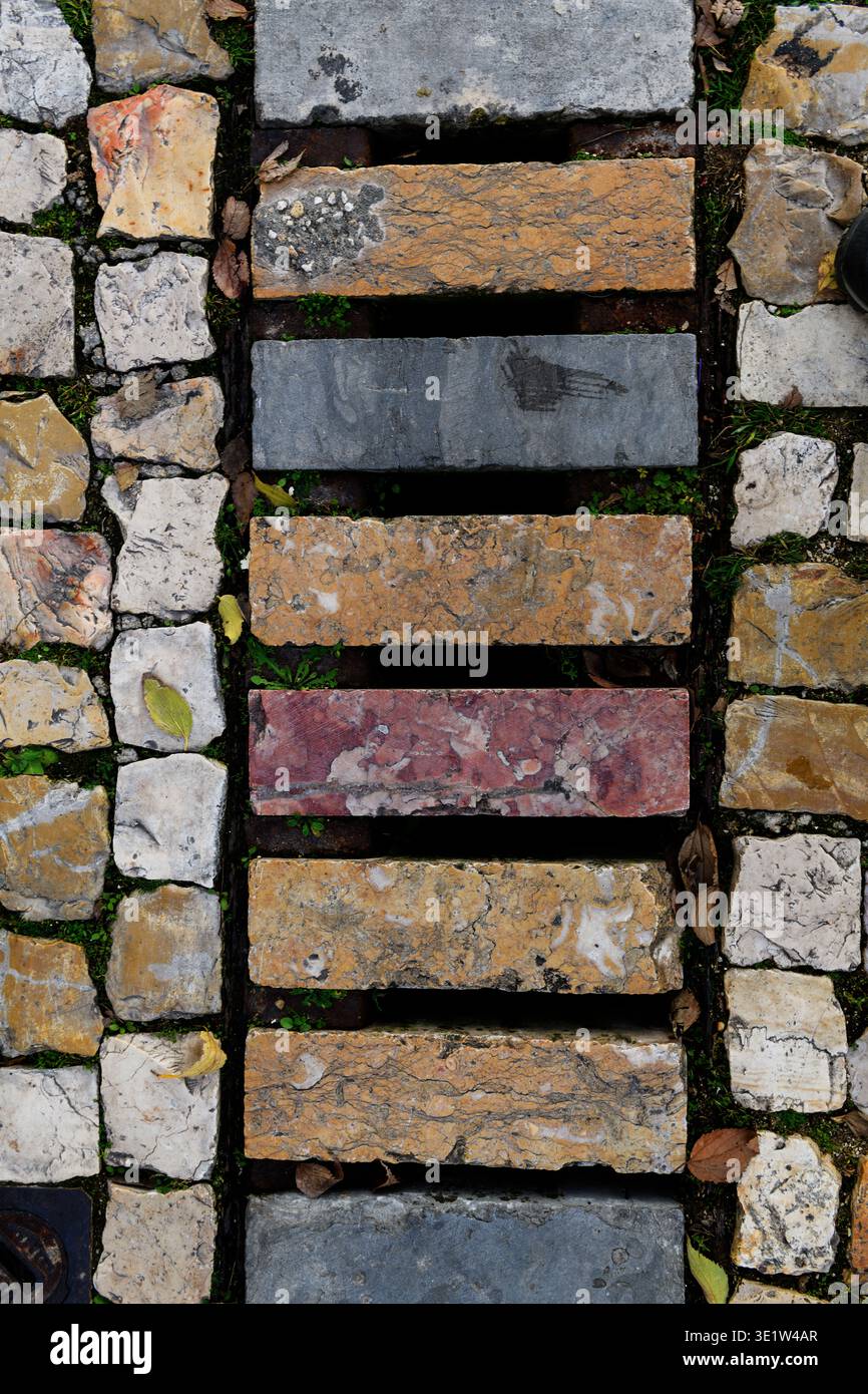 Farbenfrohe, gemusterte Steinziegel bedeckten ein Entwässerungsloch in einer alten Steinallee im historischen Viertel Alfama in Lissabon, Portugal. Stockfoto