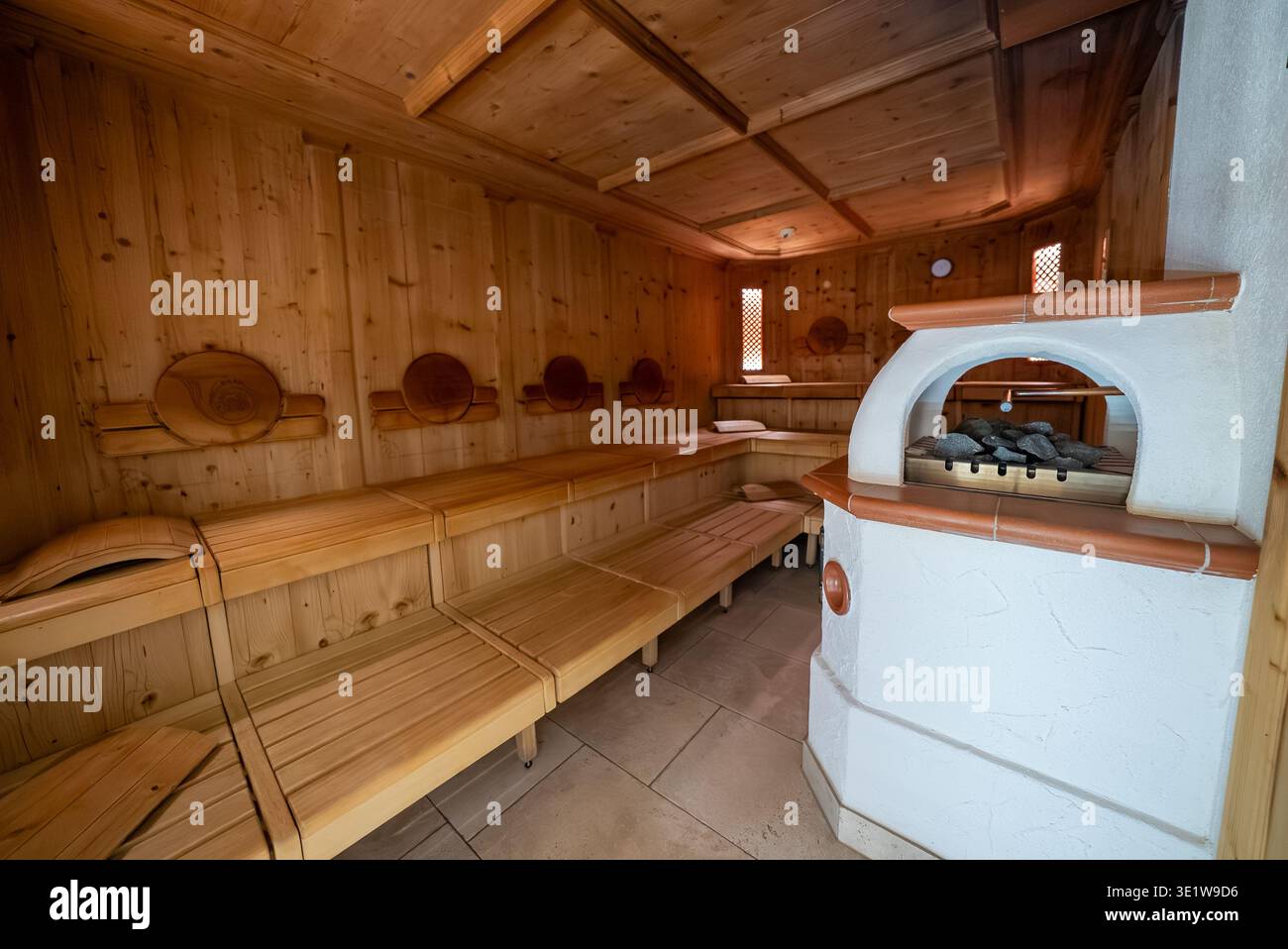 Warme Holzsauna mit Stufenbänken und weißem Stuckofen Stockfoto