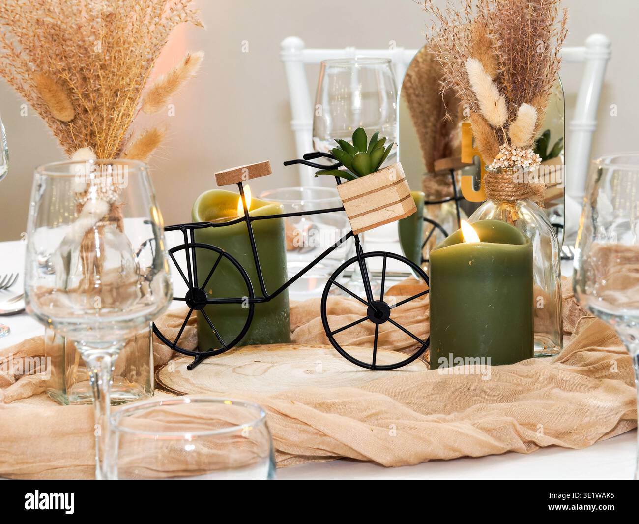 Nahaufnahme eines rustikalen Hochzeitstafels mit Kerzen, getrockneten Blumen und einem dekorativen Miniaturfahrrad. Elegante und gemütliche Tischdekoration Stockfoto