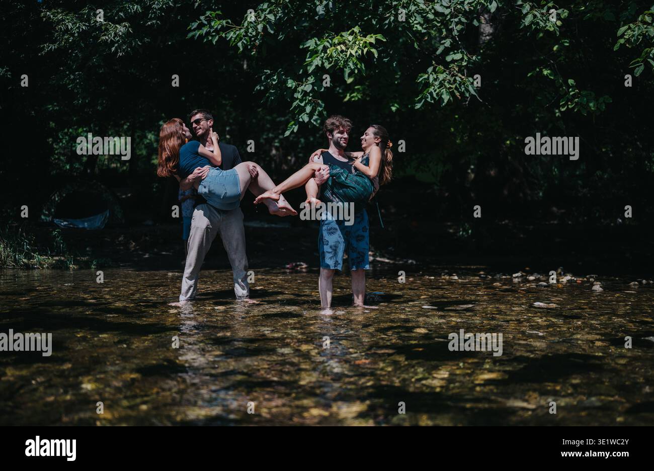 Freunde tragen sich durch einen flachen Fluss in einem sonnigen Wald und zeigen spielerische Outdoor-Bindungen Stockfoto