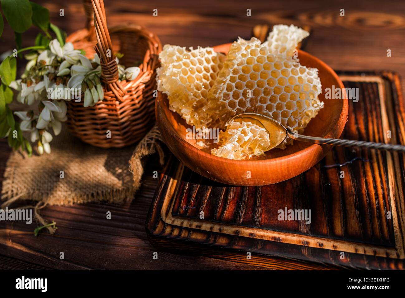 Blühender Baum zeigt duftende Blüten, die Bienen auf der Suche nach Nektar anziehen. In der Nähe befindet sich Wabenform in einer Schüssel auf einem Holztisch. Ein Korb bietet mehr Platz Stockfoto