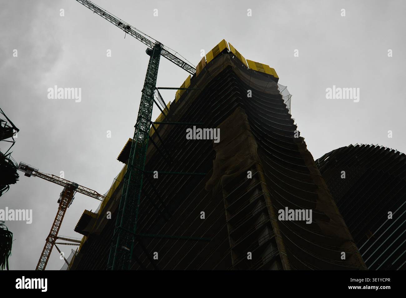 Eine professionelle architektonische Aufnahme, die die dramatische Silhouette eines im Bau befindlichen Hochhauses festnimmt. Das Bild ist grün und gelb bis Stockfoto
