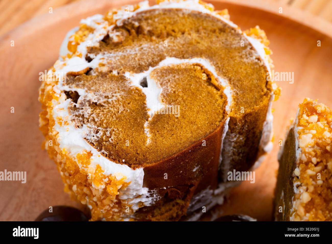 Nahaufnahme eines Kürbis-Rollkuchen mit Creme Frosting und zerstoßenen Nüssen auf einer Holzplatte Stockfoto