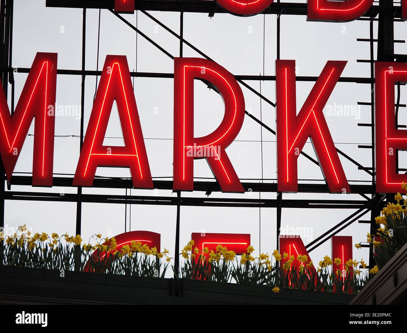 Nahaufnahme des beleuchteten Pike Place Market-Schilds im Zentrum von Seattle, Washington, USA, mit Frühlingsblumen im Vordergrund Stockfoto