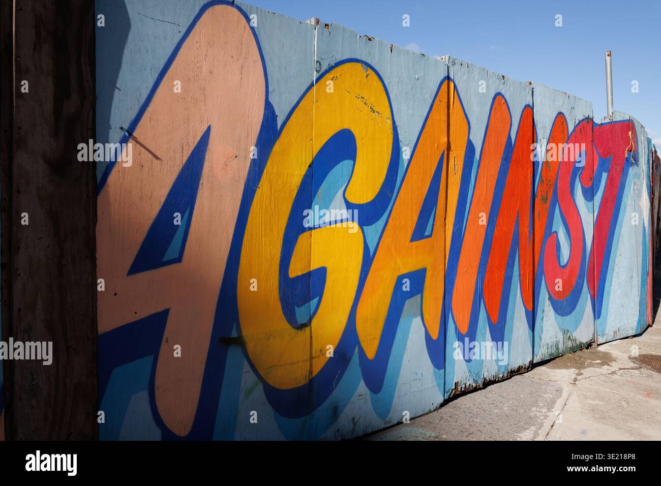 Auffälliges Graffiti-Wandbild mit der Schreibweise „AGAINST“ in mehrfarbigen Buchstaben an einer Holzwand, New York City. Stockfoto