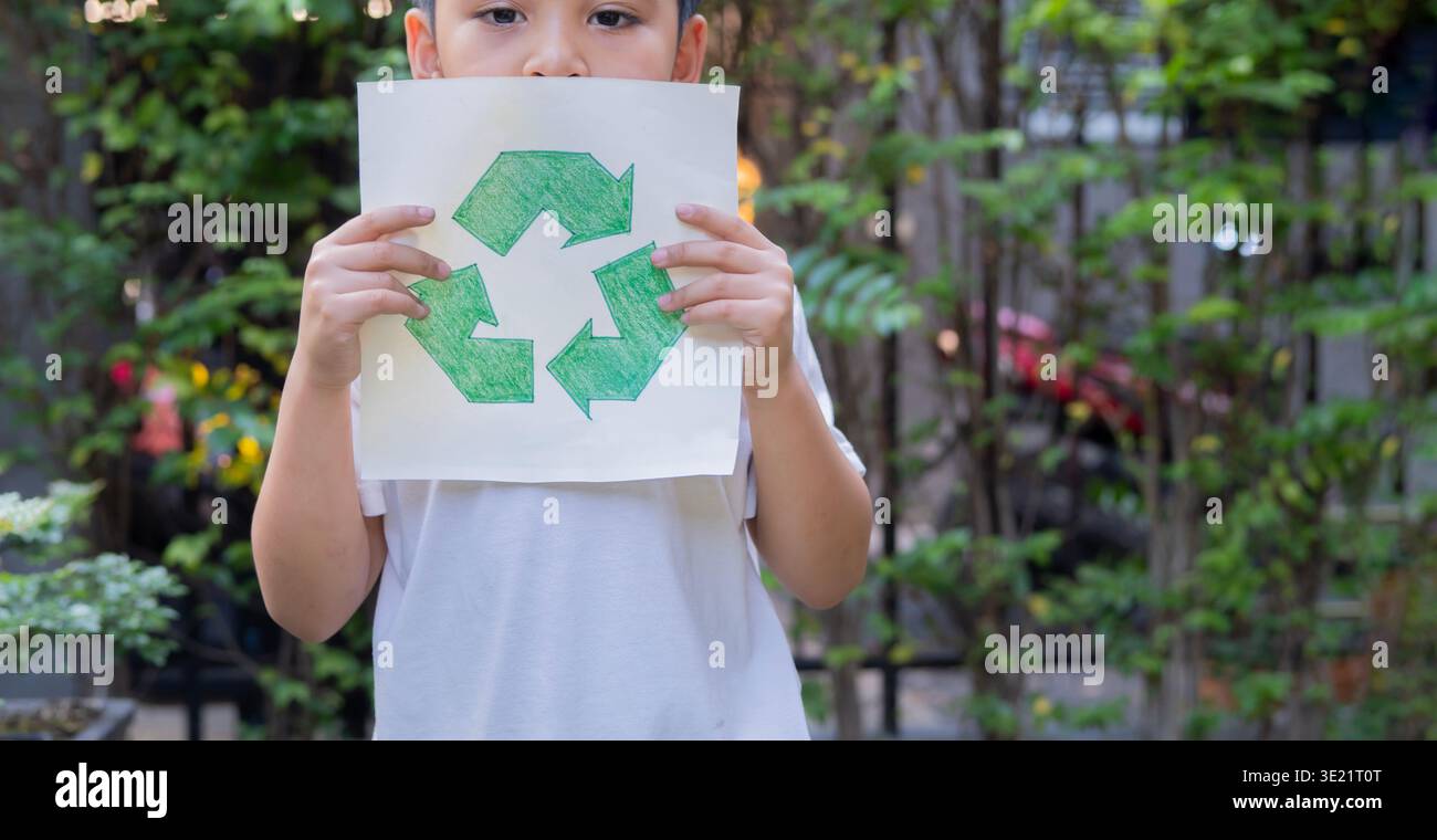 Kind hält Papier mit Recyclingschild im Freien in einem Park mit Kopierraum. Erdtag und ökologisches Konzept. Junge, der Papier recycelt, Recycling-Konzept hält Stockfoto
