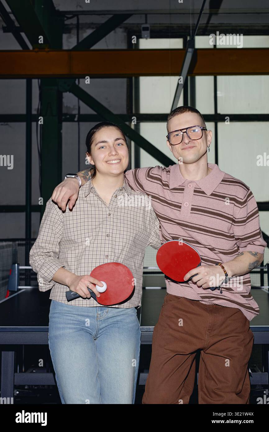 Vertikales Porträt eines jungen Mannes und einer lächelnden Frau, die Tischtennis-Paddles halten Stockfoto