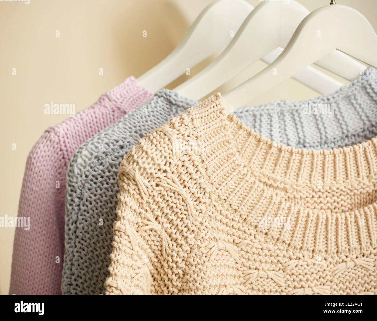 Drei Strickpullover in Pastellfarben hängen an weißen Kleiderbügeln. Deutschland Stockfoto